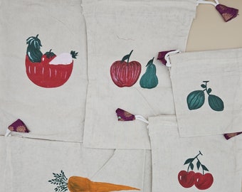 May include: Five reusable shopping bags with hand-painted fruit and vegetable designs. The bags are made of natural fabric and have a drawstring closure. The designs include a tomato, a green pepper, an apple, a pear, two green grapes, a carrot, and two red cherries.