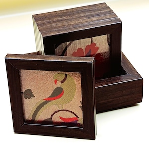 May include: A set of six wooden coasters with fabric inserts. The coasters feature a floral design and a parrot design. The coasters are stacked in a wooden box.