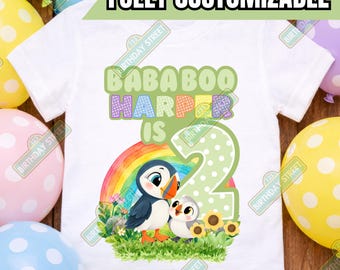 May include: A white short-sleeved t-shirt featuring a colorful graphic of a puffin and a chick standing in grass with a rainbow. The text reads BABA BOO HARPER IS 2. The design includes a large green polka-dot number two and yellow flowers.