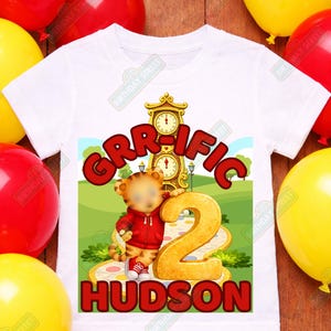 May include: White toddler t-shirt with a colorful graphic. The graphic features the word "GRR-IFIC" in red, a cartoon tiger, the number "2", and the name "HUDSON". The shirt is surrounded by red and yellow balloons.