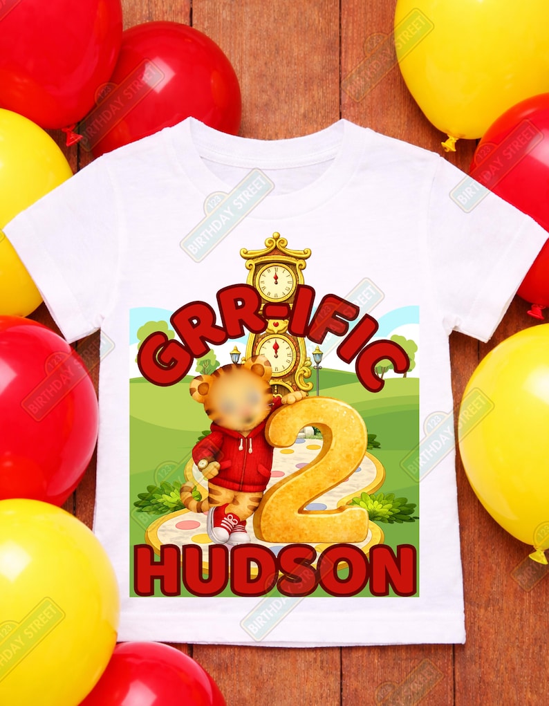 May include: White toddler t-shirt with a colorful graphic. The graphic features the word "GRR-IFIC" in red, a cartoon tiger, the number "2", and the name "HUDSON". The shirt is surrounded by red and yellow balloons.
