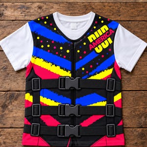 May include: A short-sleeve t-shirt featuring a white crew neck and sleeves, with a central panel displaying a vibrant pattern of blue, yellow, and pink diagonal stripes and dots. The text "NIN AMERICA UUI" is printed in yellow and pink.