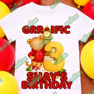 May include: White t-shirt with the text "GRR-IFIC" and "SHAY'S BIRTHDAY" in red. A cartoon bear wearing a red hoodie is featured next to a large number 3. Yellow and red balloons are in the background.