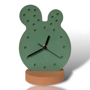 May include: A green cactus-shaped clock with black hands and a brown base.