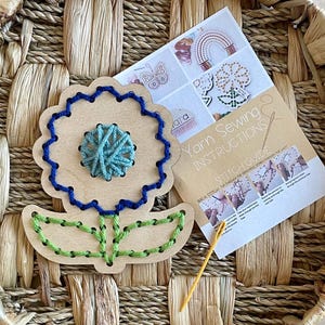 May include: A wooden flower shaped craft kit with blue, green, and brown yarn for stitching. The kit includes a needle and instructions for a back stitch.