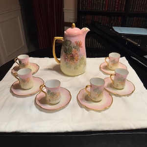 Puede incluir: Un juego de té de porcelana vintage con un diseño floral rosa y blanco. El juego incluye una tetera, un azucarero, una jarra de crema y seis tazas y platillos.