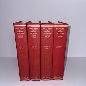 May include: Four red hardcover books titled "Encyclopedia of Frontier Biography" by Thrapp. The spines display the volume numbers and the publisher's name. The books are arranged side by side.