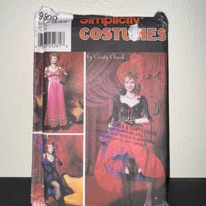 May include: Simplicity Costumes sewing pattern for a saloon girl costume. The pattern includes three different looks: a long red dress with a lace trim, a black and white dress with a lace trim, and a red skirt with a black and white top. The pattern is by Cindy Chock and is for sizes 6, 8, 10, and 12.