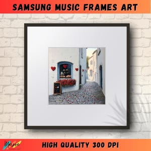 May include: A framed print of a painting depicting a narrow, cobblestone street in a European village. The street is lined with white buildings, and there is a small shop with red hearts on the window. The street is covered in red flower petals.