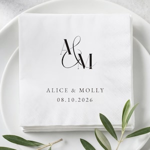 Könnte beinhalten: Eine quadratische weiße Papierserviette mit einem schwarzen Monogramm der Buchstaben A und M in einer Serifenschrift. Unter dem Monogramm steht der Text ALICE & MOLLY, gefolgt vom Datum 08.10.2026 in einer klaren, schwarzen serifenlosen Schrift.