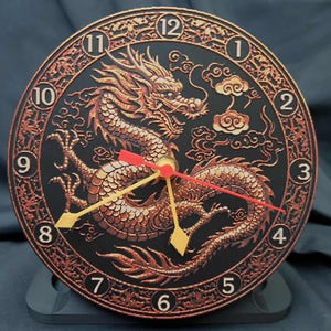 May include: A round black clock with a detailed bronze dragon design. The clock face features a dragon, clouds, and Roman numerals. The clock hands are red and yellow. The clock is on a black stand.