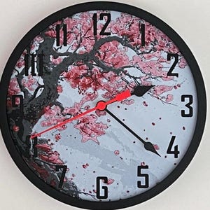 May include: Round wall clock with a black frame and a light blue face featuring a cherry blossom design. The clock hands are black with a red second hand. The numbers are black.