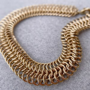 Peut inclure: Un bracelet en chaîne dorée composé d'anneaux métalliques entrelacés. Le bracelet est réalisé dans un motif tissé.