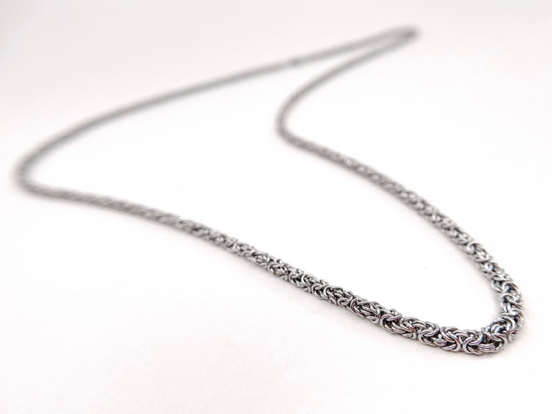 May include: A silver chain necklace with a byzantine style chain.