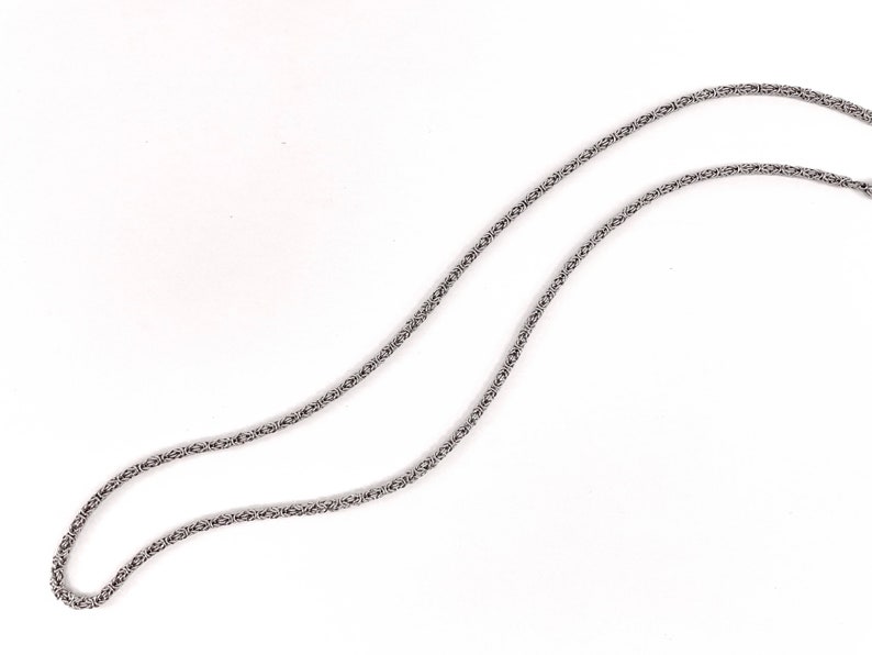 May include: A silver chain necklace with a delicate, intricate design. The chain is made of small, linked rings that create a woven pattern.
