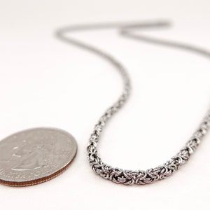 May include: A silver chain necklace with a woven design. The chain is about the size of a US quarter.