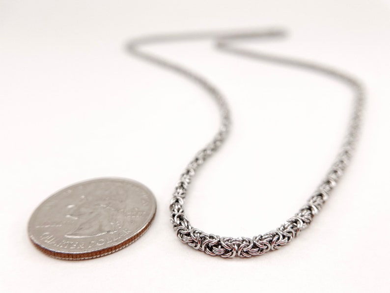 May include: A silver chain necklace with a woven design. The chain is about the size of a US quarter.
