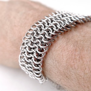 Peut inclure: Un bracelet en maille argentée avec un motif tissé. Le bracelet est porté au poignet.
