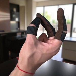 Puede incluir: Protectores de dedos con puntas de ante marrón y bandas elásticas negras. Estos protectores de dedos están diseñados para proteger los dedos durante actividades como el tiro con arco o la artesanía. Los protectores se muestran en una mano.