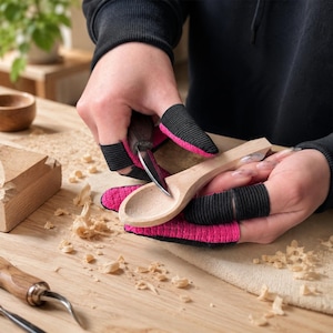Pode incluir: Um conjunto de protetores de dedos com um exterior texturizado em rosa brilhante e uma faixa elástica preta. Estes protetores são usados nos dedos enquanto se utiliza uma pequena faca de metal para esculpir uma colher de madeira clara.