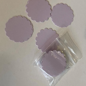 May include: A collection of lavender-colored, scalloped-edge paper circles. Four circles are scattered, with one group of circles inside a clear plastic bag. The paper has a matte finish.