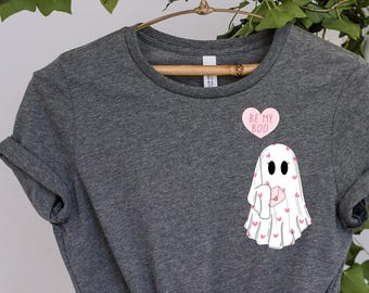 May include: A gray t-shirt with a white ghost holding a pink heart with the text "BE MY BOO" on it. The ghost is covered in pink hearts.