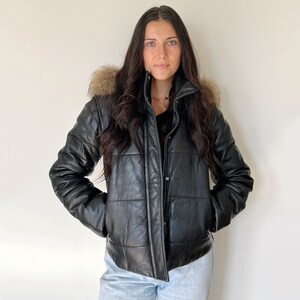 May include: A black leather puffer jacket with a faux fur hood. The jacket has a quilted design and a zipper closure.
