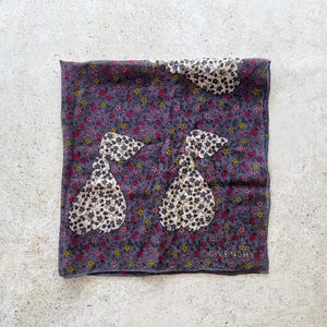 Op de afbeelding: Een donkerblauwe zijden sjaal met een bloemenpatroon en twee witte en zwarte peer-vormige ontwerpen. De sjaal heeft de tekst "Givenchy" in wit gedrukt in de rechterbenedenhoek.