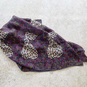 Op de afbeelding: Een donkerblauwe zijden sjaal met een bloemenpatroon en witte peer-vormige ontwerpen. De sjaal heeft het woord "Givenchy" in wit gedrukt in de rechterbenedenhoek.