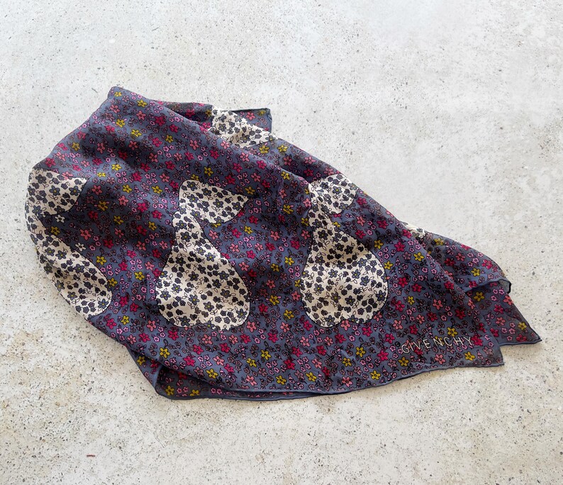 Op de afbeelding: Een donkerblauwe zijden sjaal met een bloemenpatroon en witte peer-vormige ontwerpen. De sjaal heeft het woord "Givenchy" in wit gedrukt in de rechterbenedenhoek.
