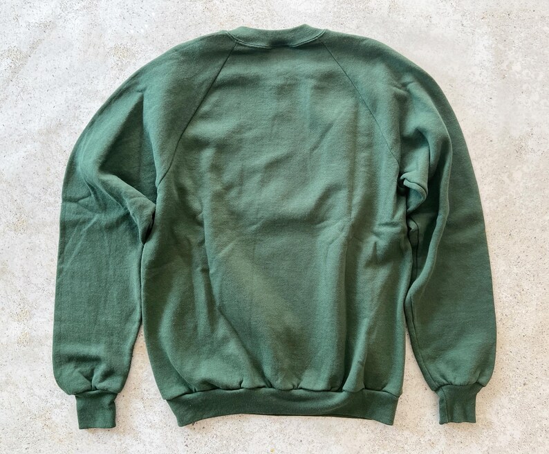 K&ouml;nnte beinhalten: Ein dunkelgr&uuml;ner Pullover mit Rundhalsausschnitt und langen &Auml;rmeln. Der Pullover hat eine klassische, lockere Passform.