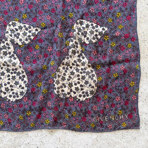 Op de afbeelding: Een blauwe zijden sjaal met een bloemenpatroon en twee peer-vormige ontwerpen. De sjaal heeft de tekst "Givenchy" gedrukt in de rechterbenedenhoek.