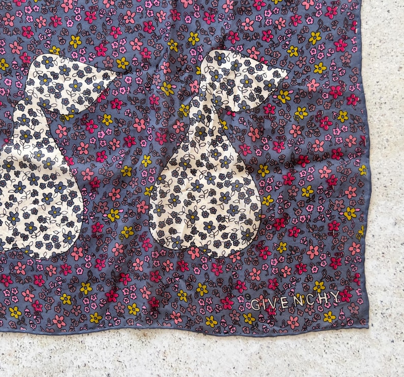 Op de afbeelding: Een blauwe zijden sjaal met een bloemenpatroon en twee peer-vormige ontwerpen. De sjaal heeft de tekst "Givenchy" gedrukt in de rechterbenedenhoek.