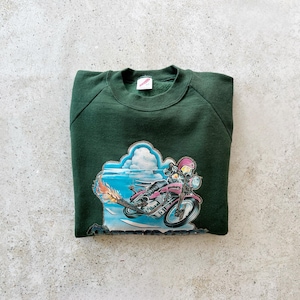 K&ouml;nnte beinhalten: Ein dunkelgr&uuml;ner Sweatshirt mit einem Aufdruck einer Person, die ein Motorrad f&auml;hrt, vor einem blauen Himmel mit Wolken.