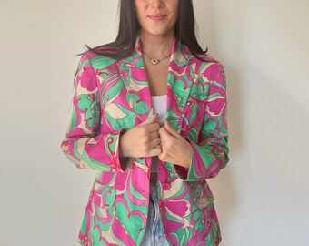 May include: A pink blazer with a green and white abstract floral pattern. The blazer has a button closure and is made of a lightweight fabric.