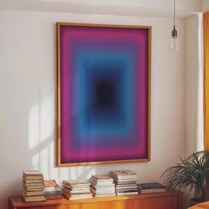 Könnte beinhalten: Ein gerahmtes abstraktes Kunstwerk mit einem Farbverlauf. Das Kunstwerk zeigt ein zentrales schwarzes Quadrat, das von Schichten aus Blau und Magenta umgeben ist, gerahmt in einem hellbraunen Holzrahmen. Das Kunstwerk hängt an einer weißen Wand.