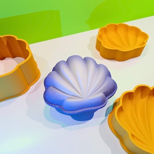 May include: Three different-sized seashell-shaped molds, one blue and two yellow. The molds are made of a smooth, rubbery material and are perfect for making cakes or other desserts.