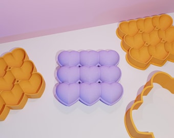 May include: Three silicone molds for baking. One mold is a square shape with nine heart-shaped cavities. The other two molds are heart-shaped and have a more intricate design.
