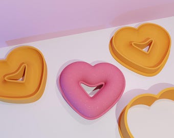 May include: Four heart-shaped cookie cutters, two are orange and two are yellow. One of the orange cutters has a pink heart inside.