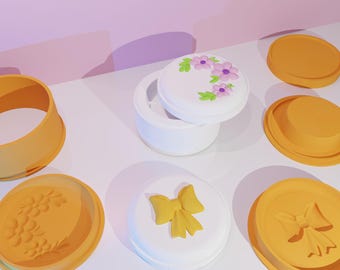 May include: A set of six round silicone molds for making decorative cakes or other treats. The molds feature different designs, including a floral wreath, a bow, and a floral pattern. The molds are white and orange.
