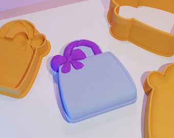 May include: A set of three cookie cutters, one shaped like a handbag with a purple bow, one shaped like a cloud, and one shaped like a heart. The cookie cutters are made of orange plastic.