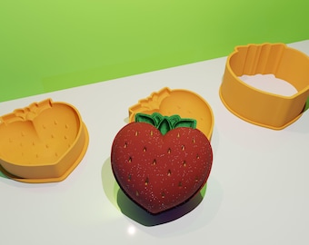 May include: Three silicone molds for baking, shaped like strawberries. The molds are yellow and red, with a green leaf detail.