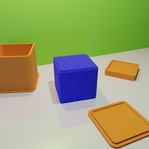 May include: Three boxes, one blue and two orange, are arranged on a white surface. The blue box is in the center and the orange boxes are on either side. The blue box has a speckled texture.