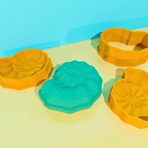 May include: Four cookie cutters in the shape of seashells. Two are yellow, one is turquoise, and one is a ring shape.