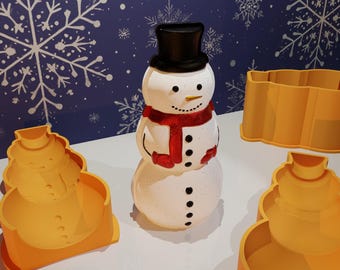 May include: A white snowman with a black top hat, red scarf, and black buttons. The snowman is surrounded by three yellow plastic molds shaped like snowmen.