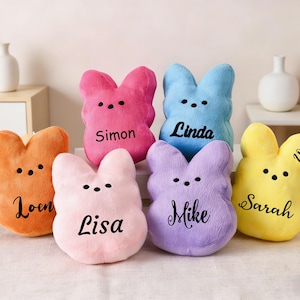 Puede incluir: Seis peluches con forma de conejito en varios colores: naranja, rosa, rosa claro, azul, morado y amarillo. Cada conejito tiene un nombre impreso en cursiva. Los conejitos tienen ojos de puntos negros.