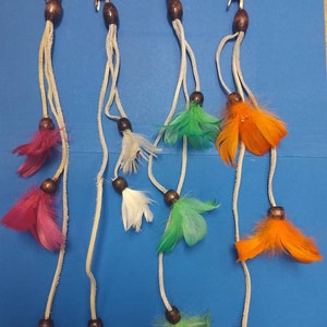 May include: Four hair clips with feathers. Each clip has a white cord with brown beads and three strands of feathers. The feathers are pink, white, green, and orange.