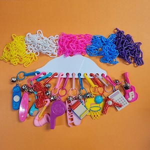 May include: A colorful plastic chain with a variety of charms attached. The charms include a skateboard, a whistle, a basketball, a calculator, a musical note, a trumpet, and a guitar. The chain is hanging from a white plastic hanger.