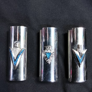 May include: Three silver cigarette lighters with blue and silver arrowhead designs.