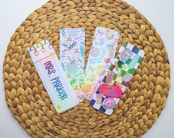 May include: Four colorful teacher-themed bookmarks with various designs, including pencils, apples, and the text "MRS. PARKER." The bookmarks are on a woven, circular surface.